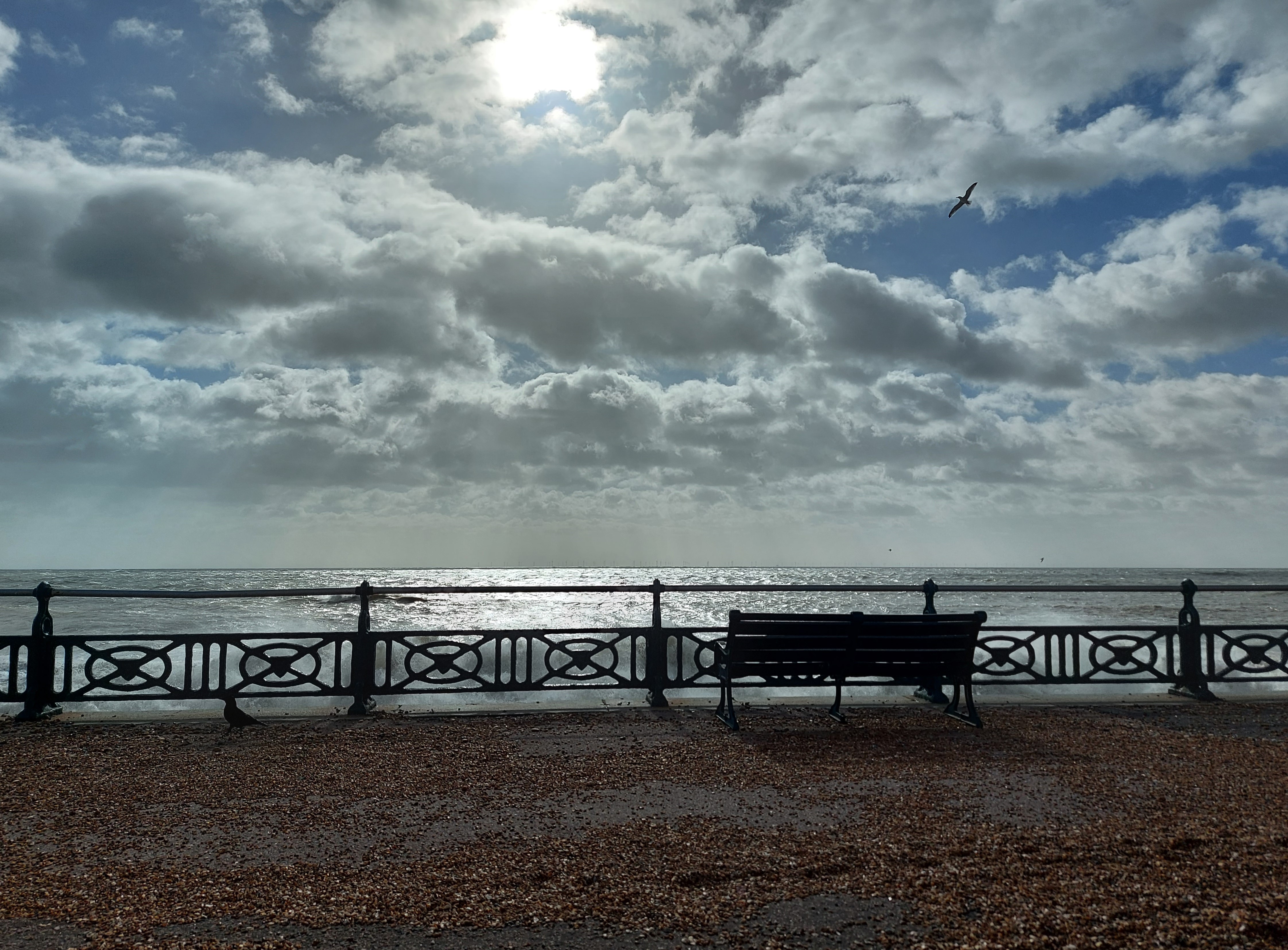 Bench on pebble-strewn footpath overlooking sea and cloudy sky